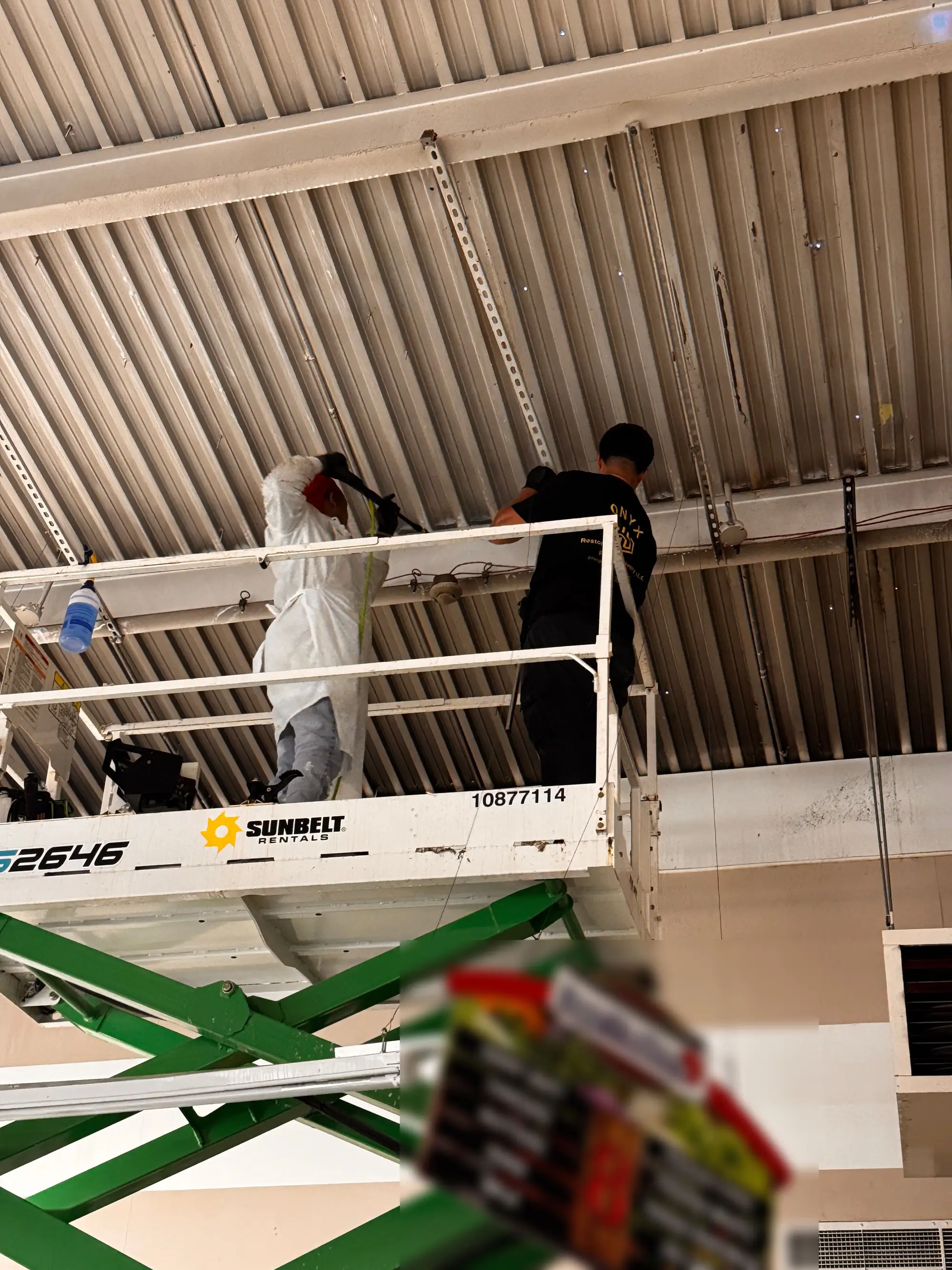 Technician in protective gear on a lift cleaning soot from a commercial ceiling after a fire