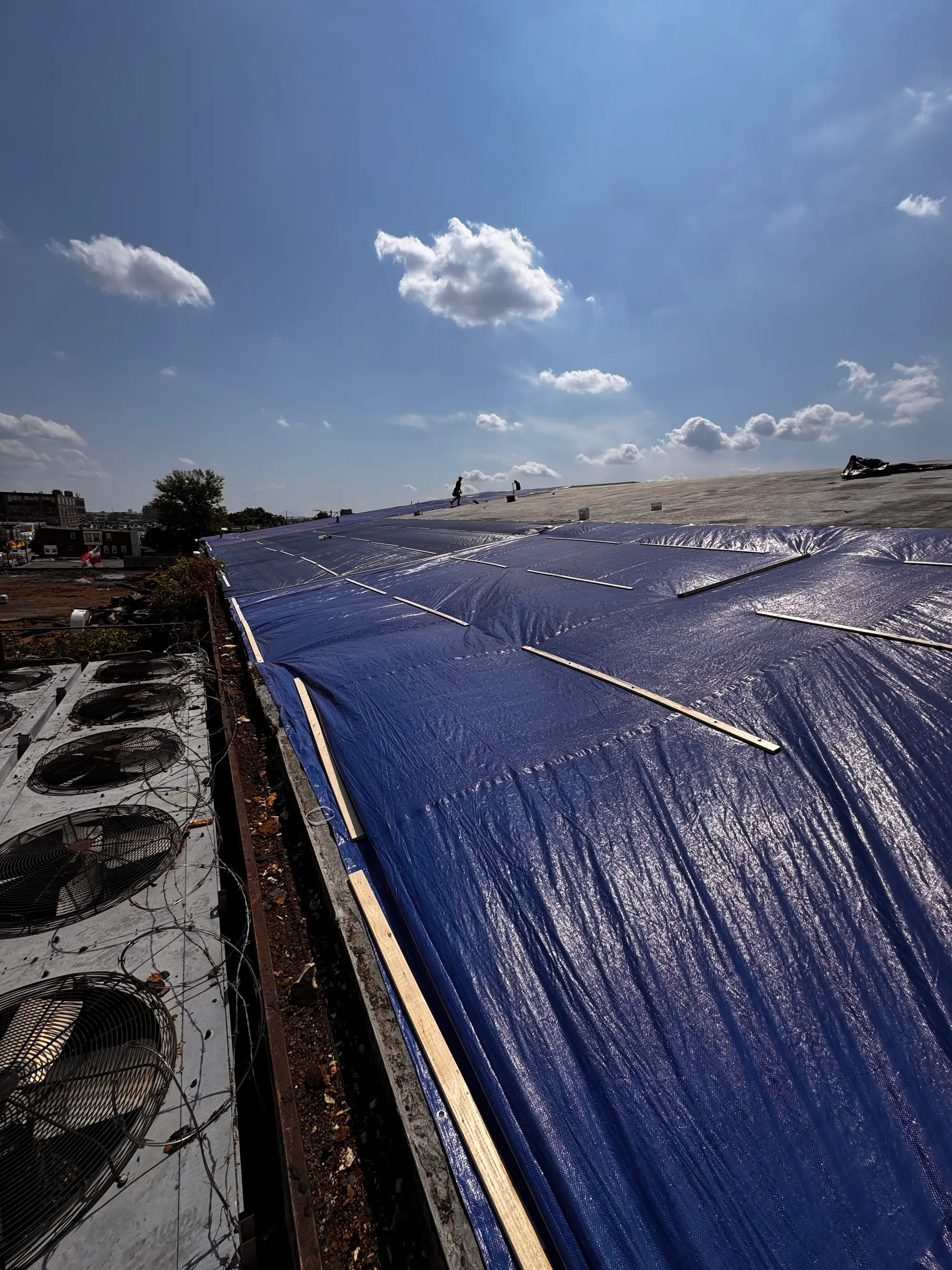 Blue emergency tarp secured over storm damage on a commercial roof beside HVAC units