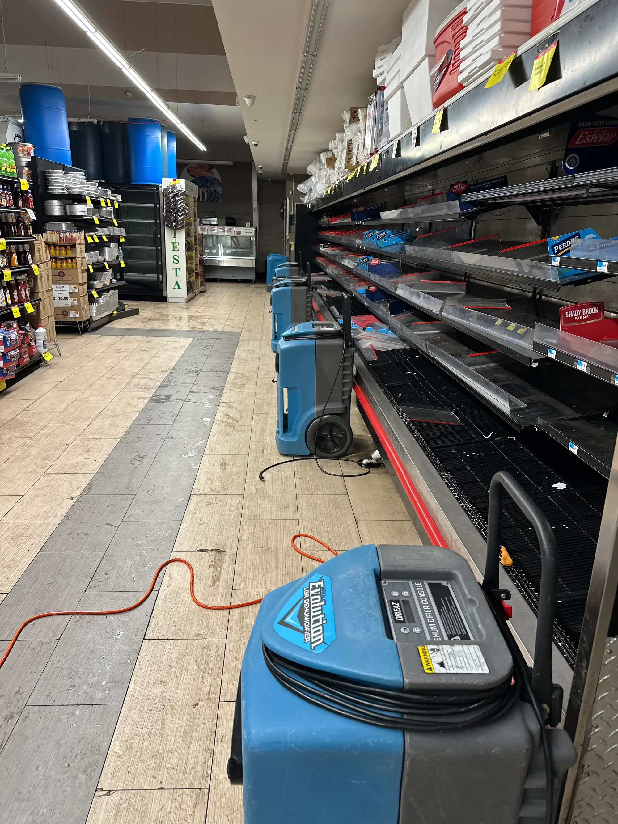 Air movers and dehumidifiers drying a commercial store aisle after water damage