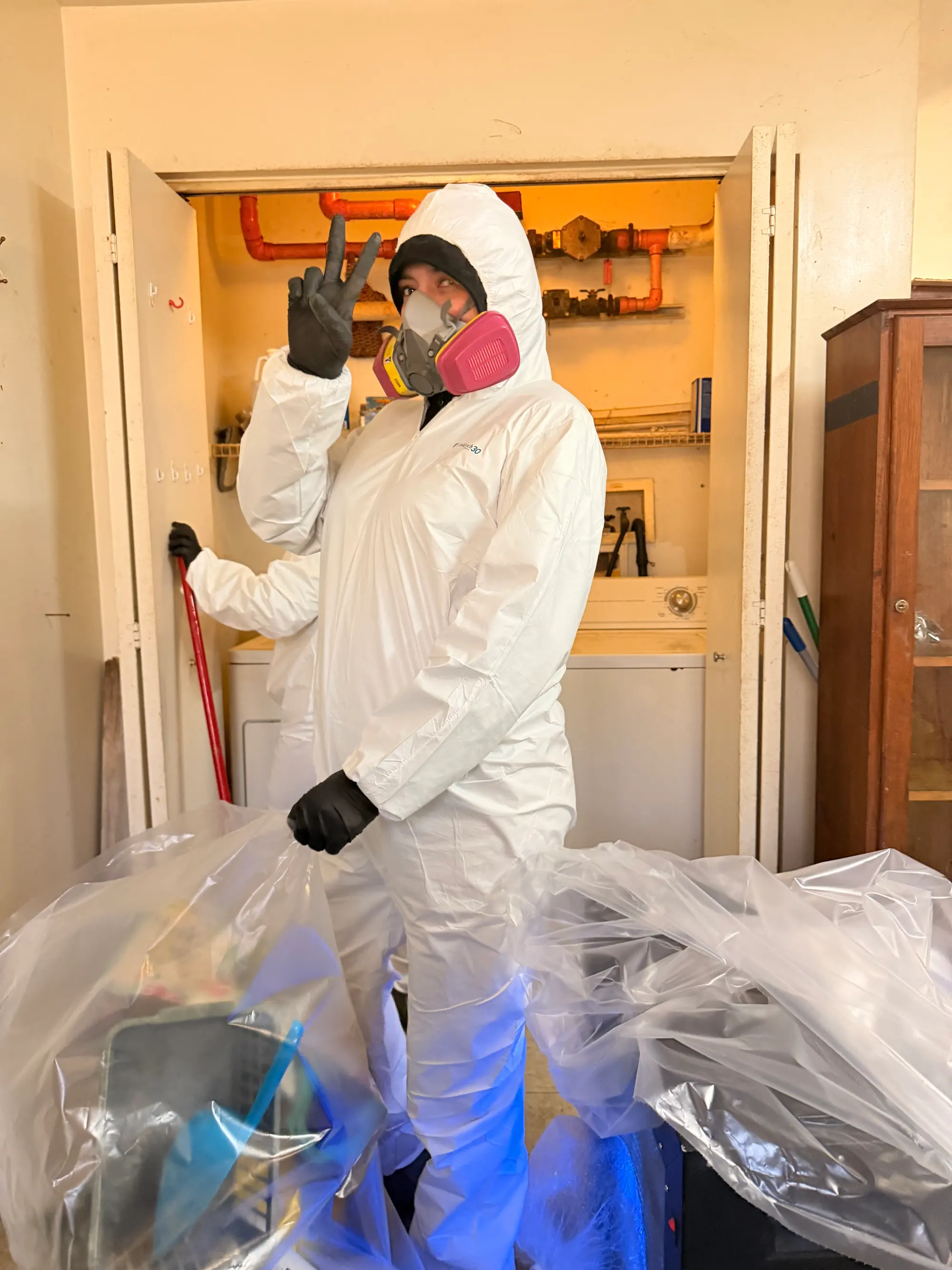 Technician in a full Tyvek suit and respirator during mold remediation in a laundry closet