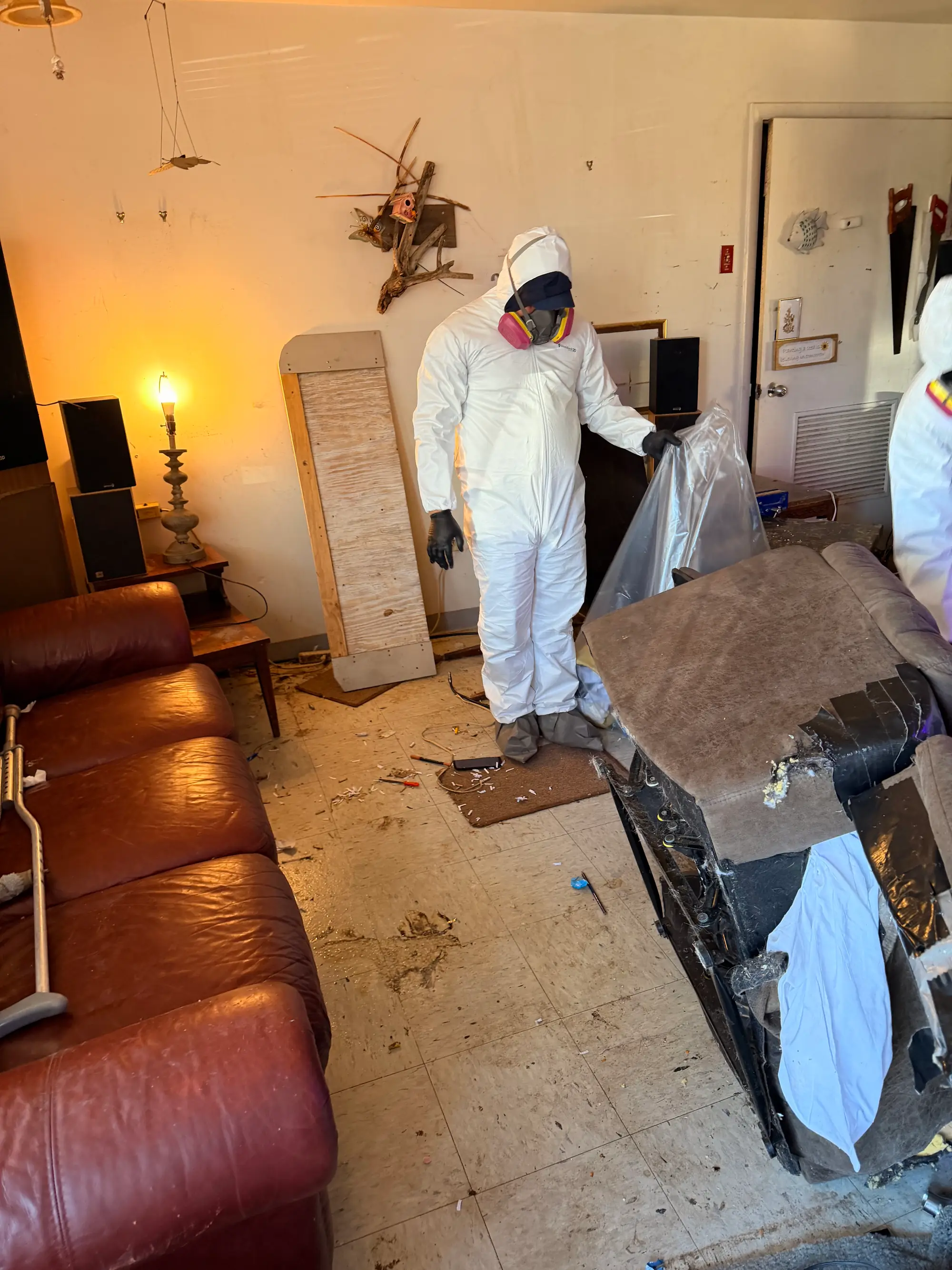 Technician in protective gear in a living room with the flooring removed during water and mold remediation