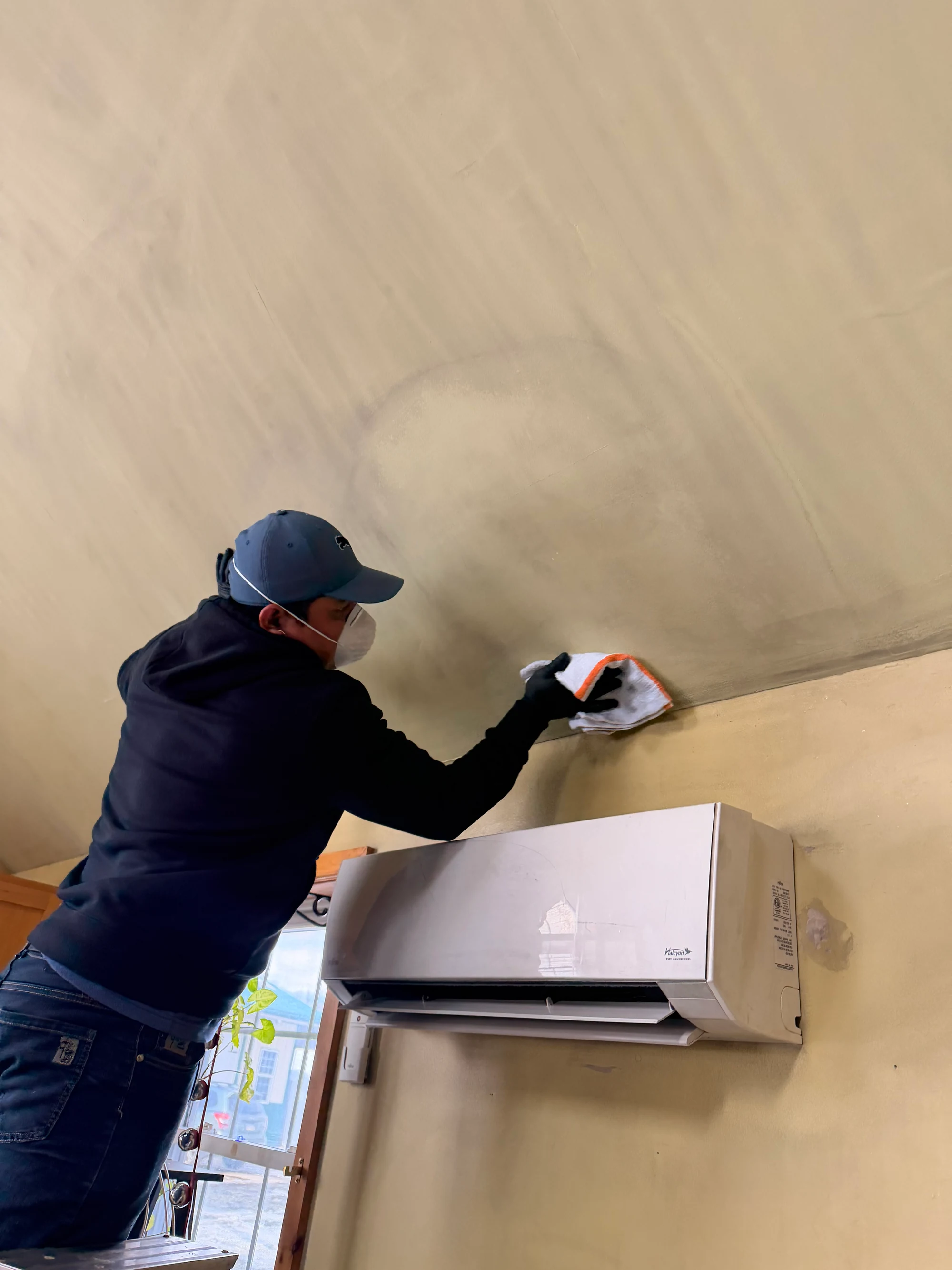 Technician wiping soot off a ceiling next to a mini-split unit during smoke damage cleanup