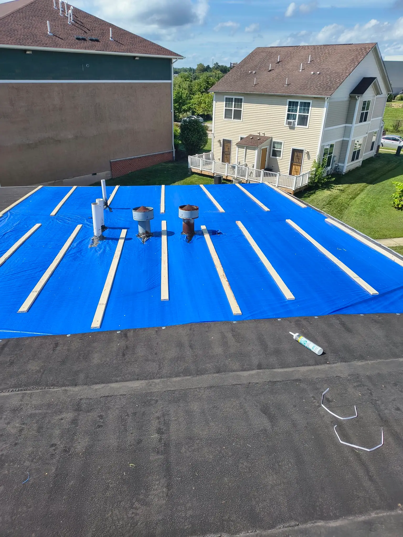 Blue emergency tarp and battens covering storm damage on a townhouse roof