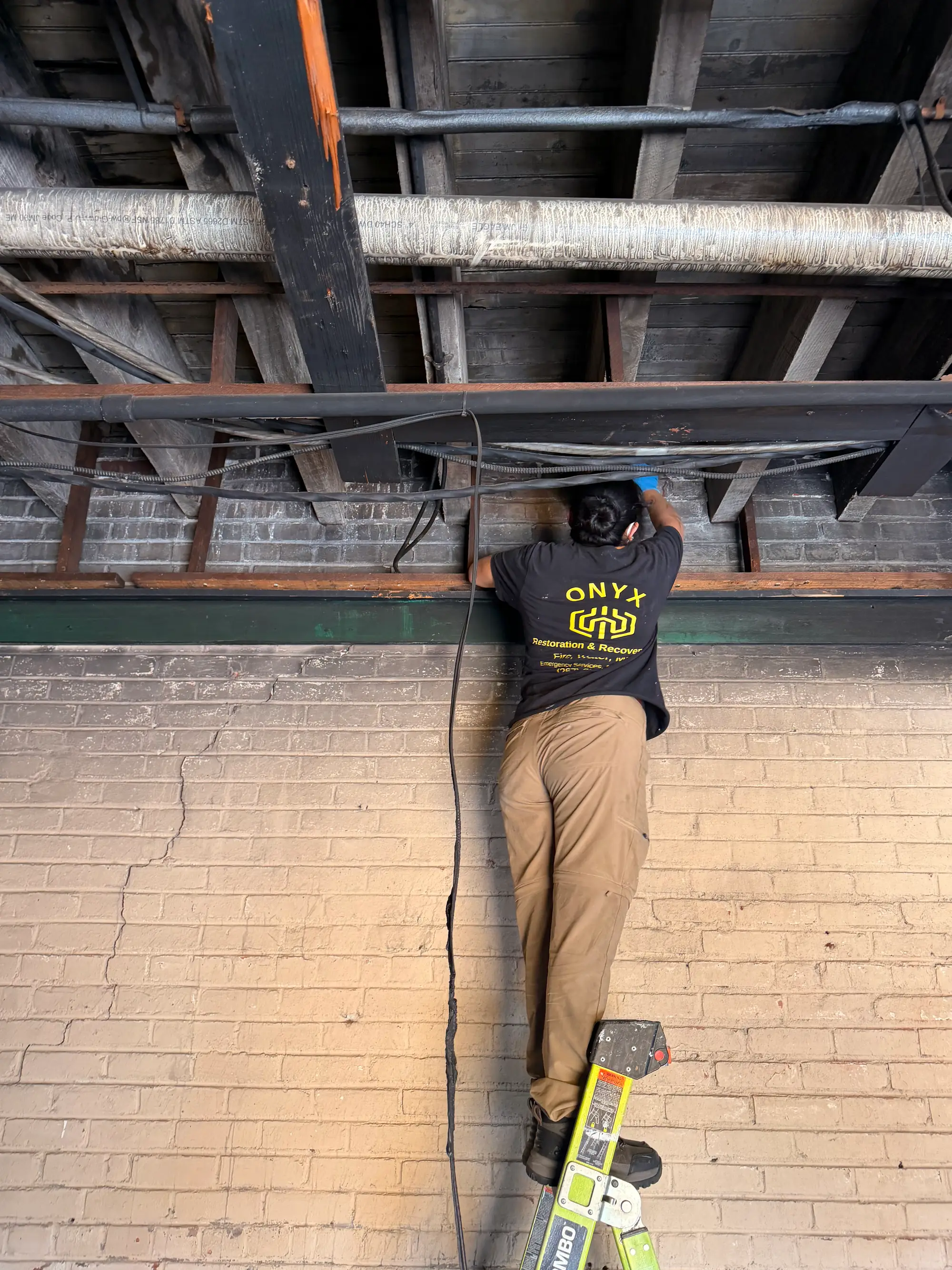 Onyx crew member on a ladder inspecting exposed ceiling joists in a commercial space